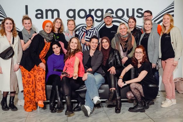 Gruppenfoto von Frauen in bunt gestalteter Umgebung, die fröhlich lächeln.